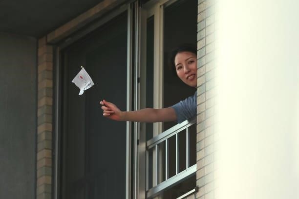 Resident waves a flag out their window as athletes compete in the Women's Marathon Final on day fifteen of the Tokyo 2020 Olympic Games at Sapporo...