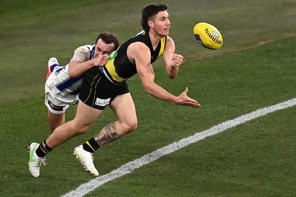Liam Baker of the Tigers handballs whilst being tackled by Jack Mahony of the Kangaroos during the round 21 AFL match between Richmond Tigers and...