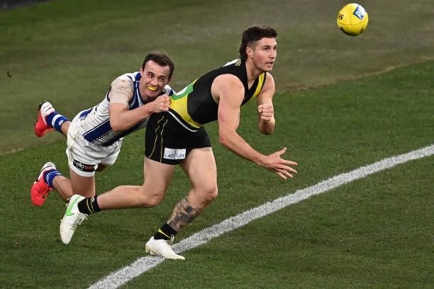 Liam Baker of the Tigers handballs whilst being tackled by Jack Mahony of the Kangaroos during the round 21 AFL match between Richmond Tigers and...