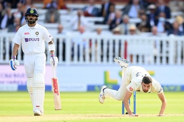 Mark Wood of England falls over after bowling as Virat Kohli looks on during the 2nd LV= Test match between England and India at Lord's Cricket...