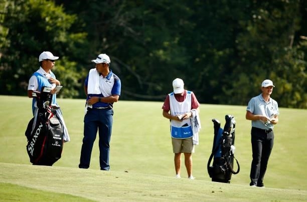 Hideki Matsuyama of Japan talks with caddie Shota Hayafuji as Justin Rose of England and his caddie look on from the 14th fairway during the first...