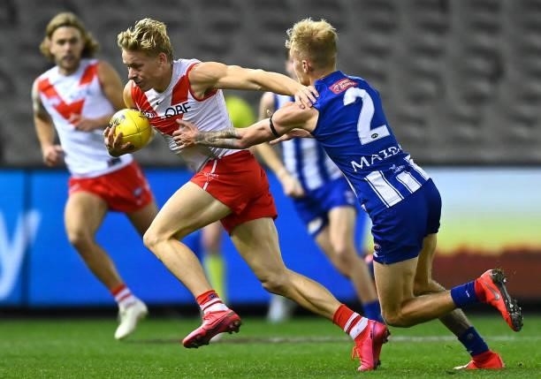 Isaac Heeney of the Swans fends off a tackle by Jaidyn Stephenson of the Kangaroos during the round 22 AFL match between North Melbourne Kangaroos...