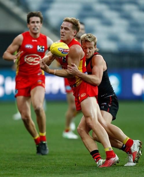 Darcy Macpherson of the Suns handballs as Darcy Parish of the Bombers applies a tackle during the round 22 AFL match between Gold Coast Suns and...