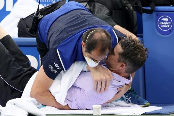 John Isner receives treatment from ATP trainer Alejandro Resnicoff while playing Cameron Norrie of Great Britain during the Western & Southern Open...