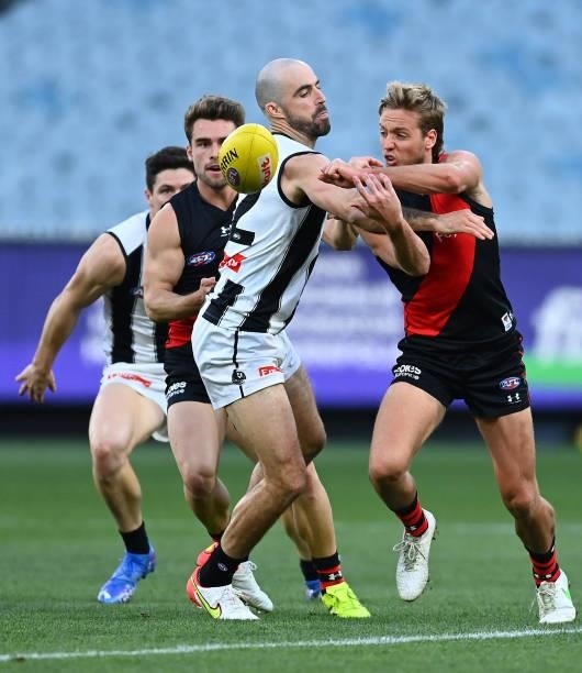 Darcy Parish of the Bombers handballs as he is tackled by Steele Sidebottom of the Magpies during the round 23 AFL match between Essendon Bombers and...