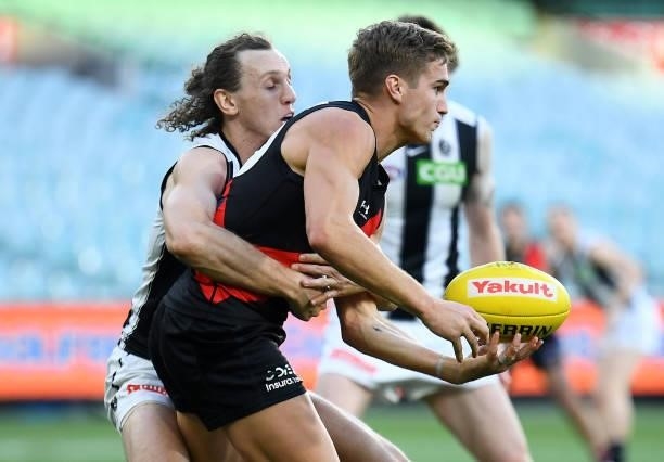 Matt Guelfi of the Bombers handballs whilst being tackled by Chris Mayne of the Magpies during the round 23 AFL match between Essendon Bombers and...
