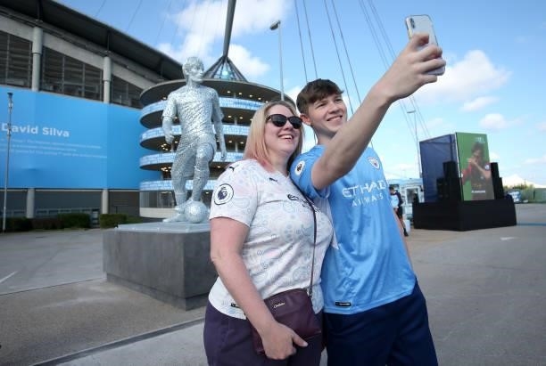 Fans pose with a statue of David Silva of Manchester City that is seen outside the stadium prior to the Premier League match between Manchester City...