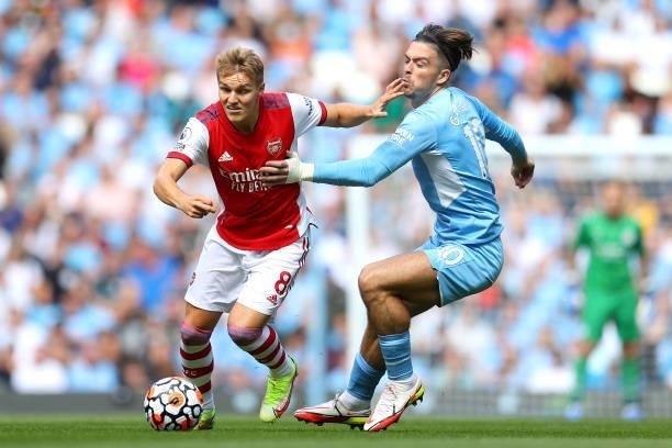Martin Odegaard of Arsenal is challenged by Jack Grealish of Manchester City during the Premier League match between Manchester City and Arsenal at...