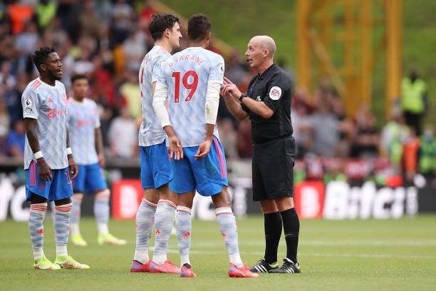 Match Referee Mike Dean interacts with Harry Maguire and Raphaël Varane of Manchester United during the Premier League match between Wolverhampton...