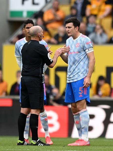 Match Referee Mike Dean interacts with Harry Maguire and Raphaël Varane of Manchester United during the Premier League match between Wolverhampton...