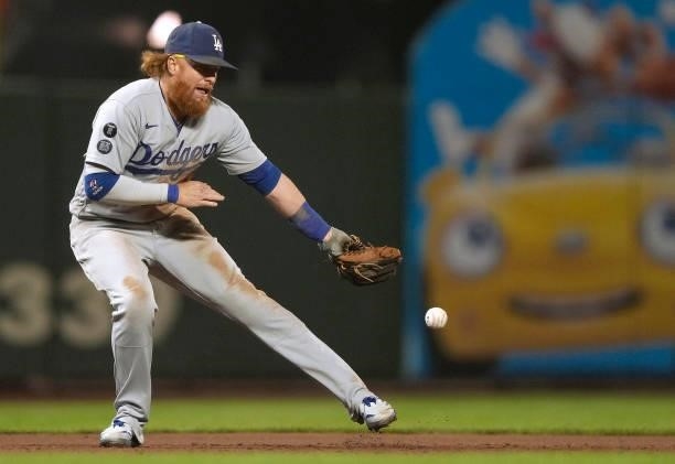 Justin Turner of the Los Angeles Dodgers watches the ball kick off his glove for a base hit off the bat of Kris Bryant of the San Francisco Giants in...