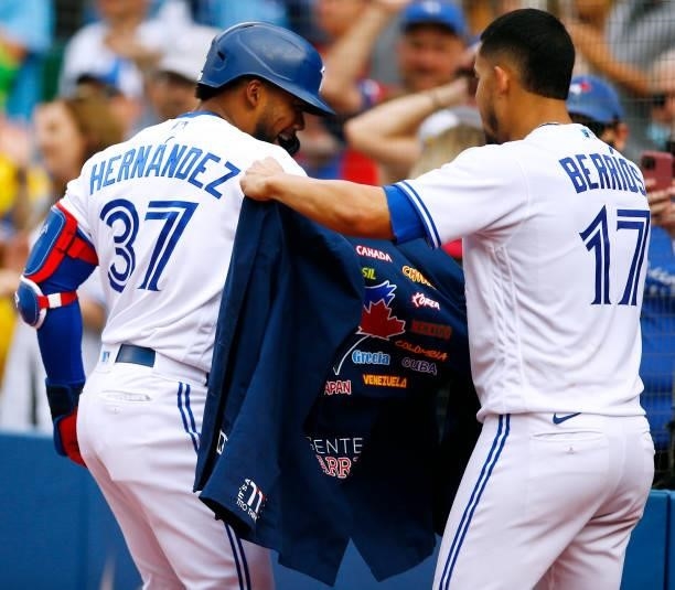 Teoscar Hernandez of the Toronto Blue Jays is given the Blue Jays home run jacket by Jose Berrios after hitting his 100th career home run during a...