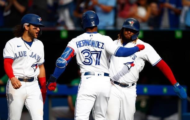 Teoscar Hernandez of the Toronto Blue Jays celebrates with Bo Bichette and Vladimir Guerrero Jr. #27 after hitting his 100th career home run during a...