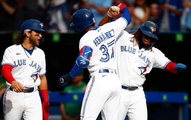 Teoscar Hernandez of the Toronto Blue Jays celebrates with Bo Bichette and Vladimir Guerrero Jr. #27 after hitting his 100th career home run during a...