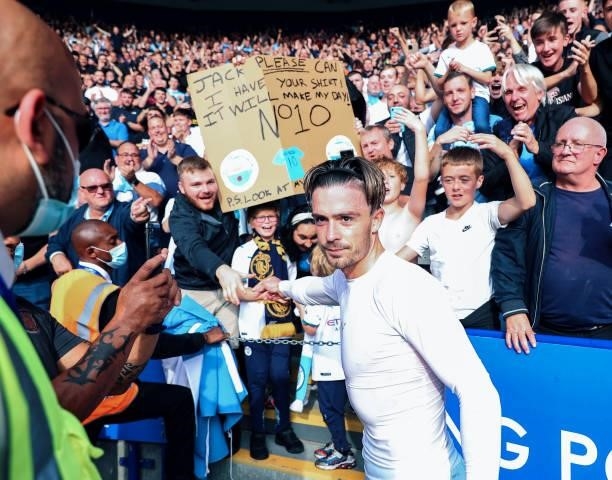 Jack Grealish of Manchester City hands his shirt to a young fan during the Premier League match between Leicester City and Manchester City at The...