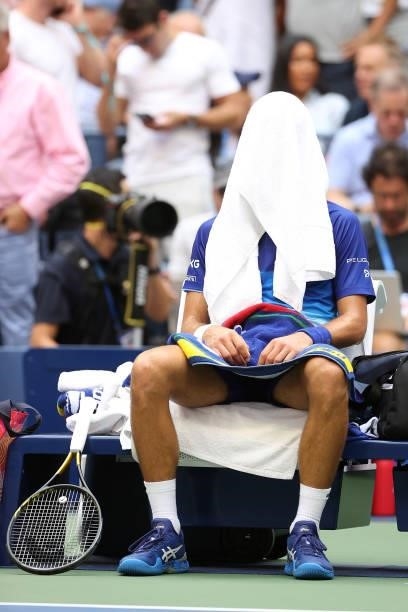 Novak Djokovic of Serbia sits under a towel in his chair between games against Daniil Medvedev of Russia during their Men's Singles final match on...