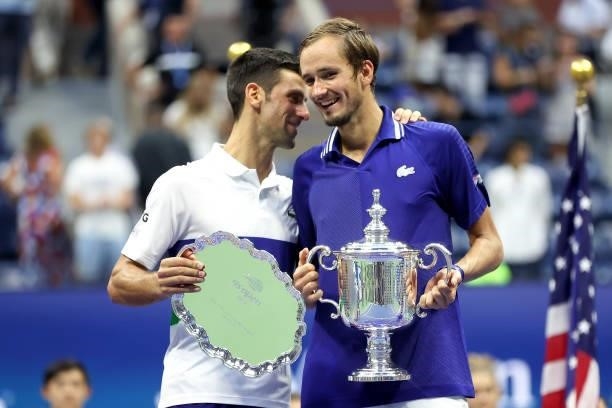 Novak Djokovic of Serbia holds the runner-up trophy and talks with Daniil Medvedev of Russia who celebrates with the championship trophy after...