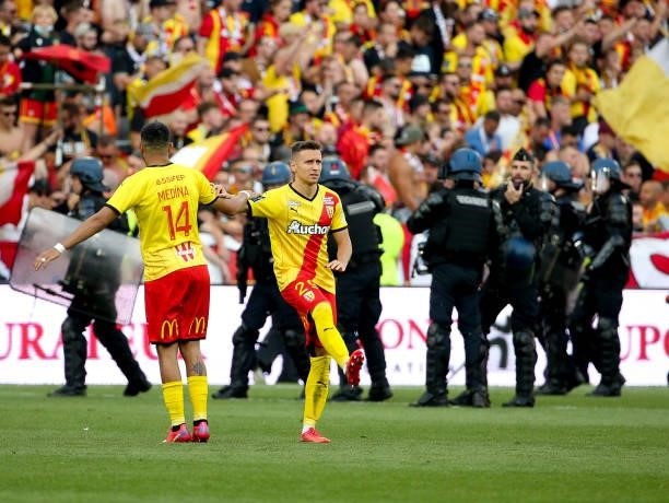 Facundo Medina and Przemyslaw Frankowski of Lens warm up while police forces protect the pitch after incidents between supporters of Lens and Lille...