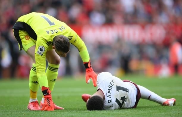 An injured Jacob Ramsey of Aston Villa is checked on by David De Gea of Manchester United during the Premier League match between Manchester United...
