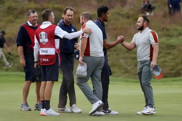 Shane Lowry of Ireland and team Europe and Tyrrell Hatton of England and team Europe shake hands with Tony Finau of team United States and Harris...
