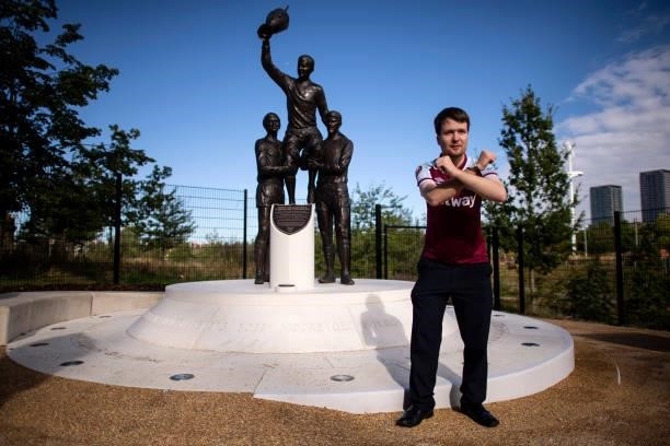 View of a fan posing with a statue of former West Ham United players, Martin Peters, Bobby Moore and Geoff Hurst celebrating winning the 1965...