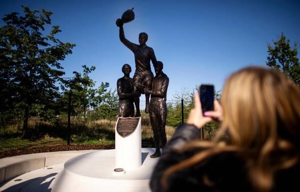 View of a fan taking a photo of a statue of former West Ham United players, Martin Peters, Bobby Moore and Geoff Hurst celebrating winning the 1965...