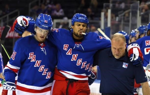 Ryan Reaves of the New York Rangers is escorted off the ice following an injury during the first period by Sammy Blais and trainer Jim Ramsay during...