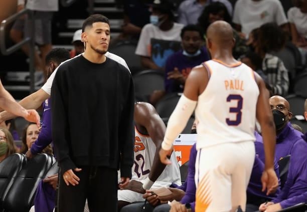 Devin Booker of the Phoenix Suns greets Chris Paul as he walks to the bench during the NBA preseason game at Footprint Center on October 06, 2021 in...