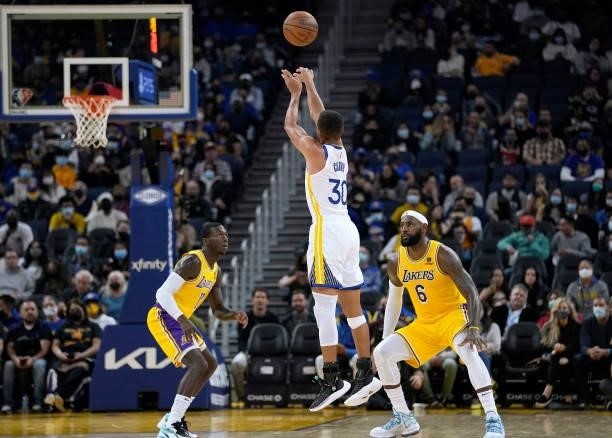 Stephen Curry of the Golden State Warriors shoots a three-point shot over LeBron James and Kendrick Nunn of the Los Angeles Lakers at Chase Center on...