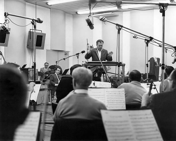 American arranger, composer and bandleader Nelson Riddle conducts an orchestra in a studio, circa 1965.