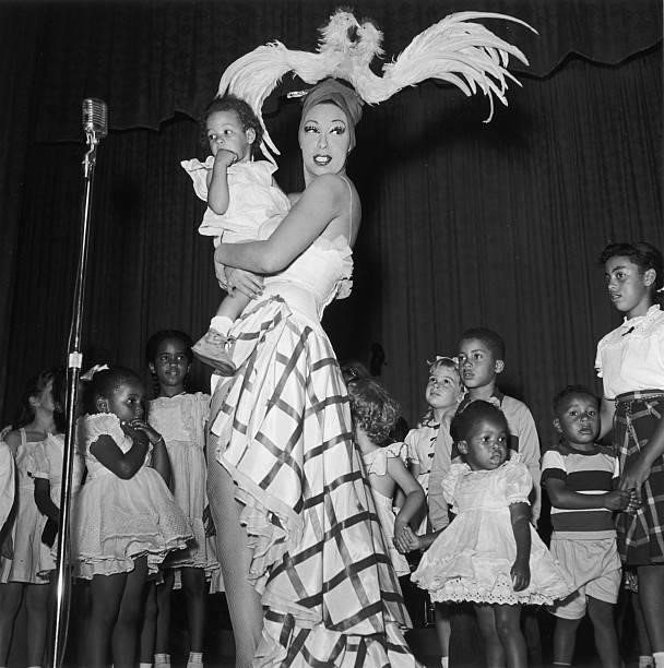 American-born singer and dancer Josephine Baker stands on stage, holding a young child, as a group of children stand behind her, Los Angeles,...