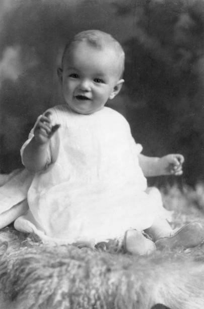 Studio portrait of American actor Marilyn Monroe at the age of six months, sitting on a woolly rug in a white smock.