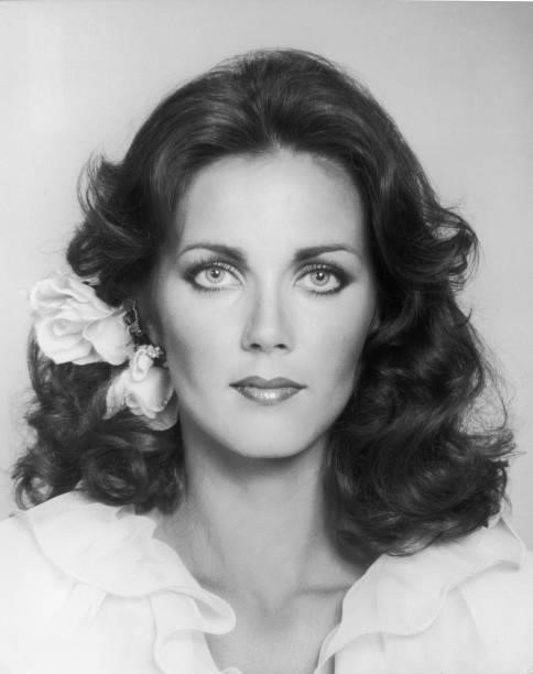 Closeup portrait of American actor Lynda Carter wearing a flower behind her ear and a ruffle-collared shirt.