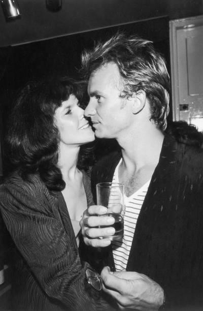 British rock musician Sting, wearing a sweater over a striped shirt, holds a drink and looks to the side as his first wife, actor Frances Tomelty,...