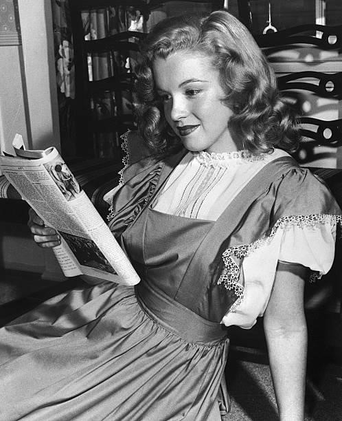Marilyn Monroe at 21, reading a magazine and wearing a demure dress. Her hair is still long and undyed.