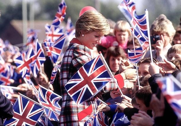 The Princess of Wales walks amongst crowds of children waving flags during her visit to Cullompton in Devon, September 1990. She is wearing a...