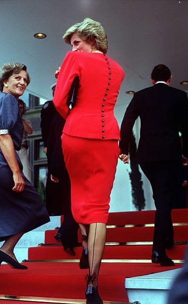 The Princess of Wales wearing a red suit and tights with a decorative bow at the ankle during a visit to parliament in Camberra, January 1988.