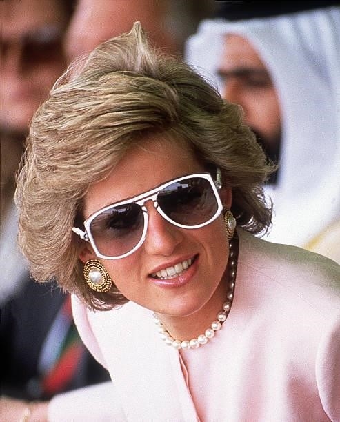 Princess Diana, wearing a Catherine Walker suit and white sunglasses, watching camel racing at Al Maqam during an official visit to Abu Dhabi, March...