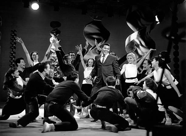 American rock 'n roll singer and dancer, Chubby Checker, performing with a group of dancers, circa 1964. The set is decorated with 'twist'...