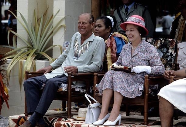 Queen Elizabeth II, holding her gold Rollei camera, and Prince Philip, Duke of Edinburgh, wearing a traditional shell necklace watch traditional...